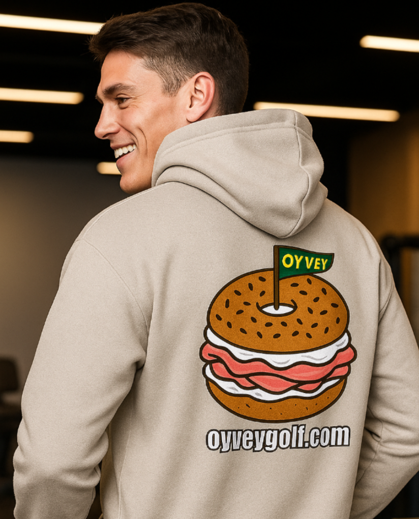 Man wearing a hoodie with a bagel graphic and 'Oyvey Golf' branding.